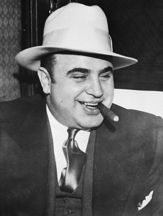 Infamous gangster Al Capone smokes a cigar on the train carrying him to the federal penitentiary in Atlanta where he will start serving an eleven-year sentence.