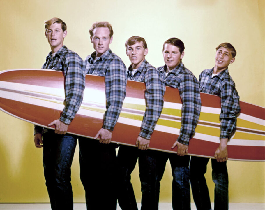 Rock and roll band "The Beach Boys" pose for a portrait with a surfboard in August 1962 in Los Angeles, California. (L-R) Brian Wilson, Mike Love, Dennis Wilson, Carl Wilson, David Marks. This image was used on the cover of 'Surfin' USA'.