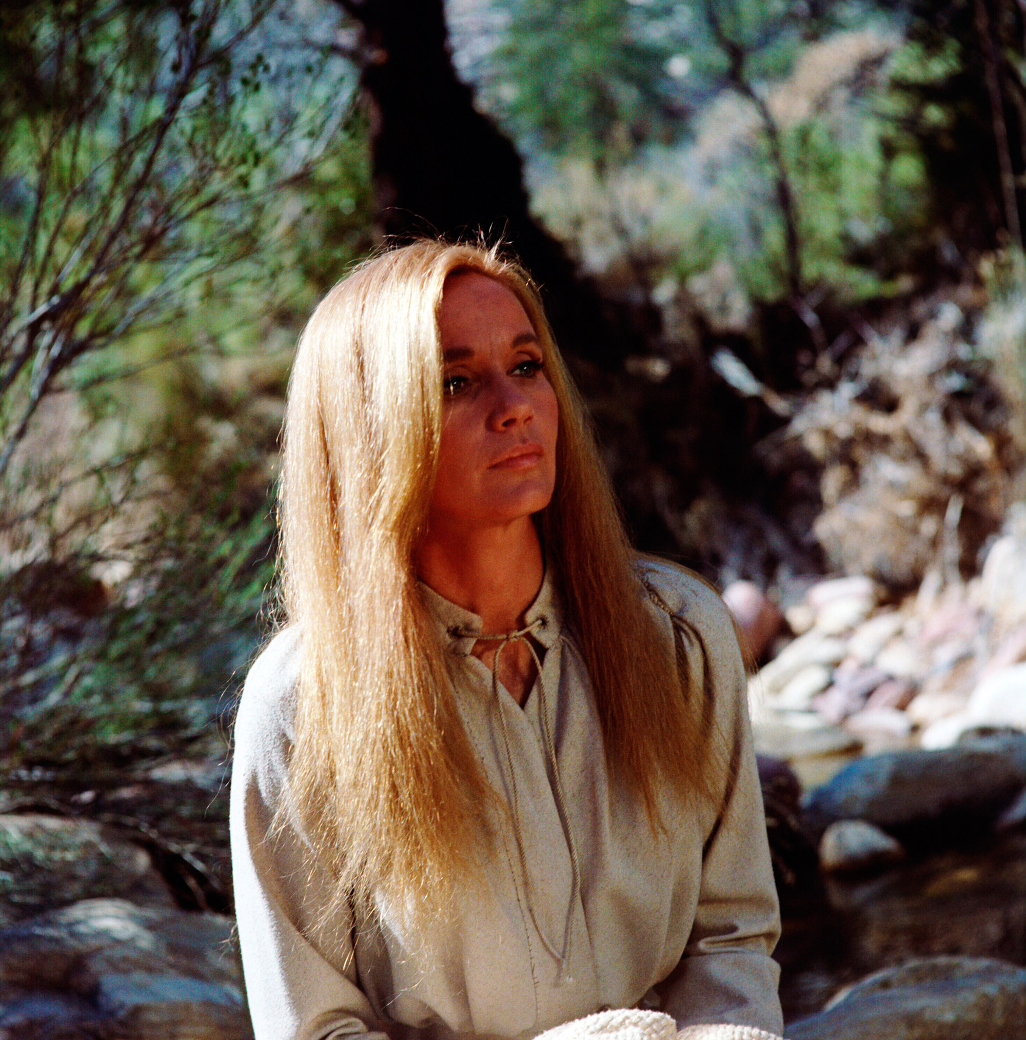 color image from the 1968 Western movie "The Stalking Moon." Star Eva Marie Saint is depicted as her 19th-century character, wearing a white shirt and with long blond hair. She is seated in a wilderness area.