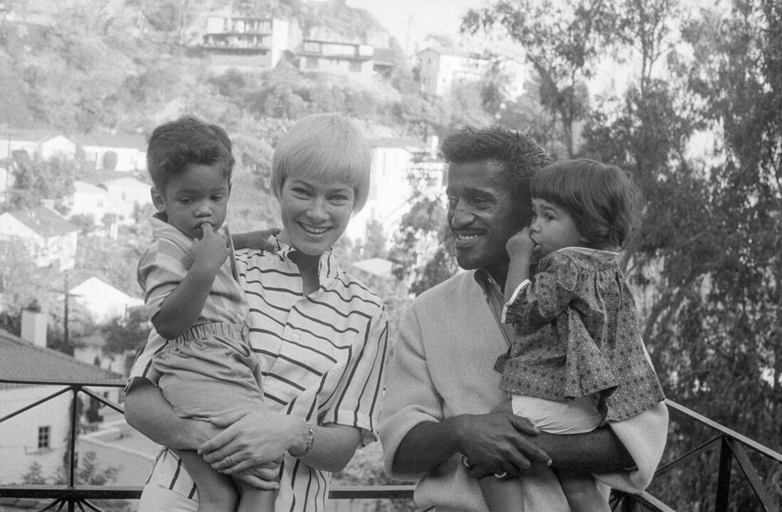 (Original Caption) Sammy Davis, Jr., and Family. Hollywood, California: Versatile entertainer Sammy Davis, Jr., and his wife, actress May Britt, pose with their newly enlarged family in the garden of their home November 10th. The couple recently adopted a son whom they named Mark Sidney Davis (left). Sammy holds their 16-month-old daughter, Tracey Hillivi. He said, "We love children. When our house becomes too small, we'll build a bigger one"