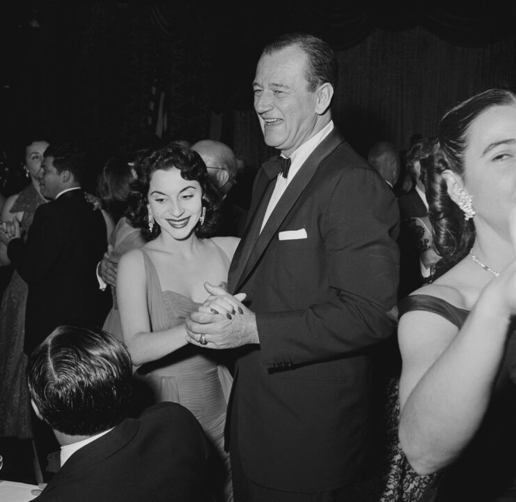 Peruvian actress Pilar Pallete and her husband, American actor John Wayne (1907-1979), both smiling as they dance at an event, United States, circa 1955.